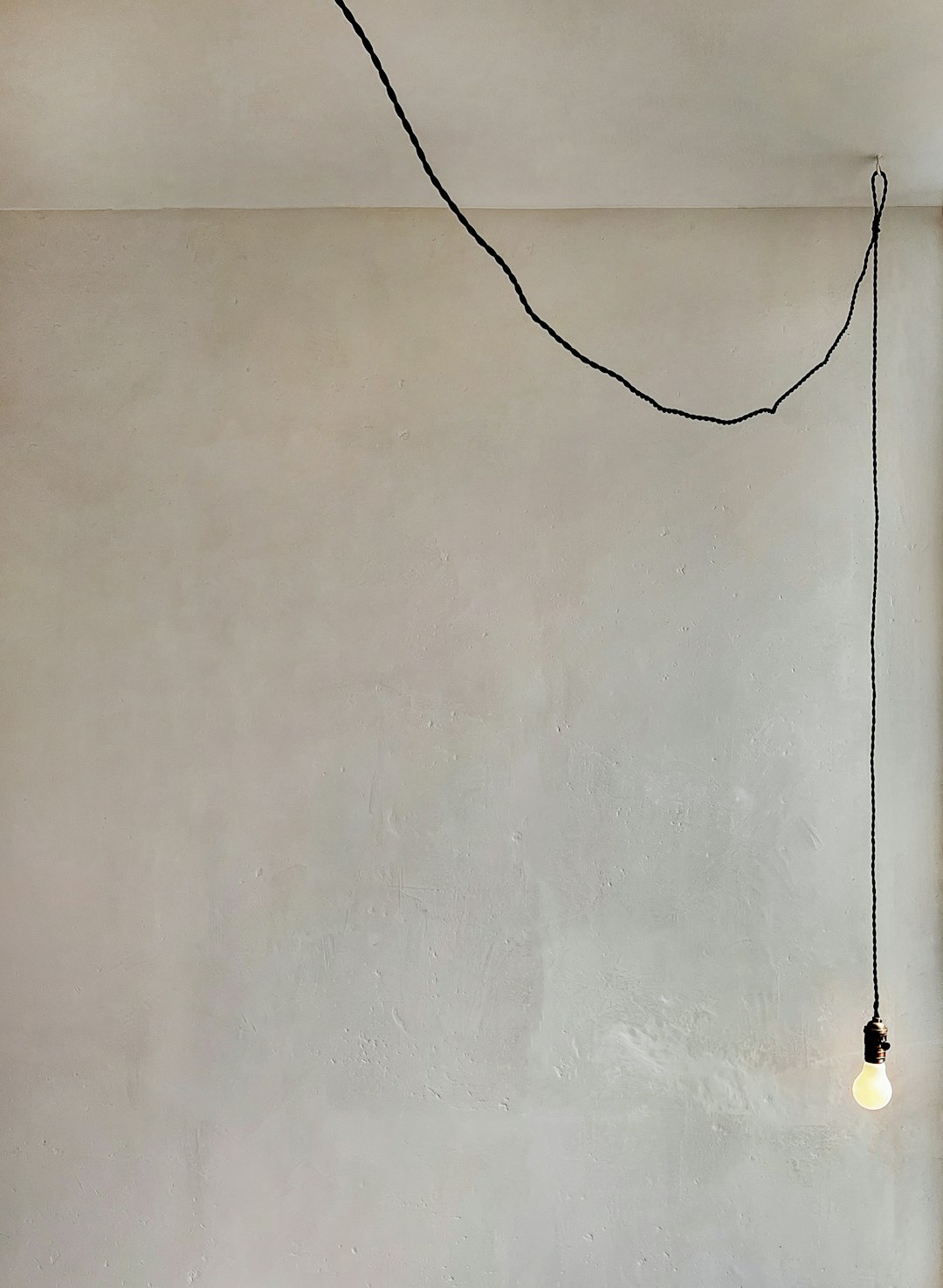 a-room-with-a-white-wall-and-a-black-string-hanging-from-the-ceiling-mnwyidwc2vo